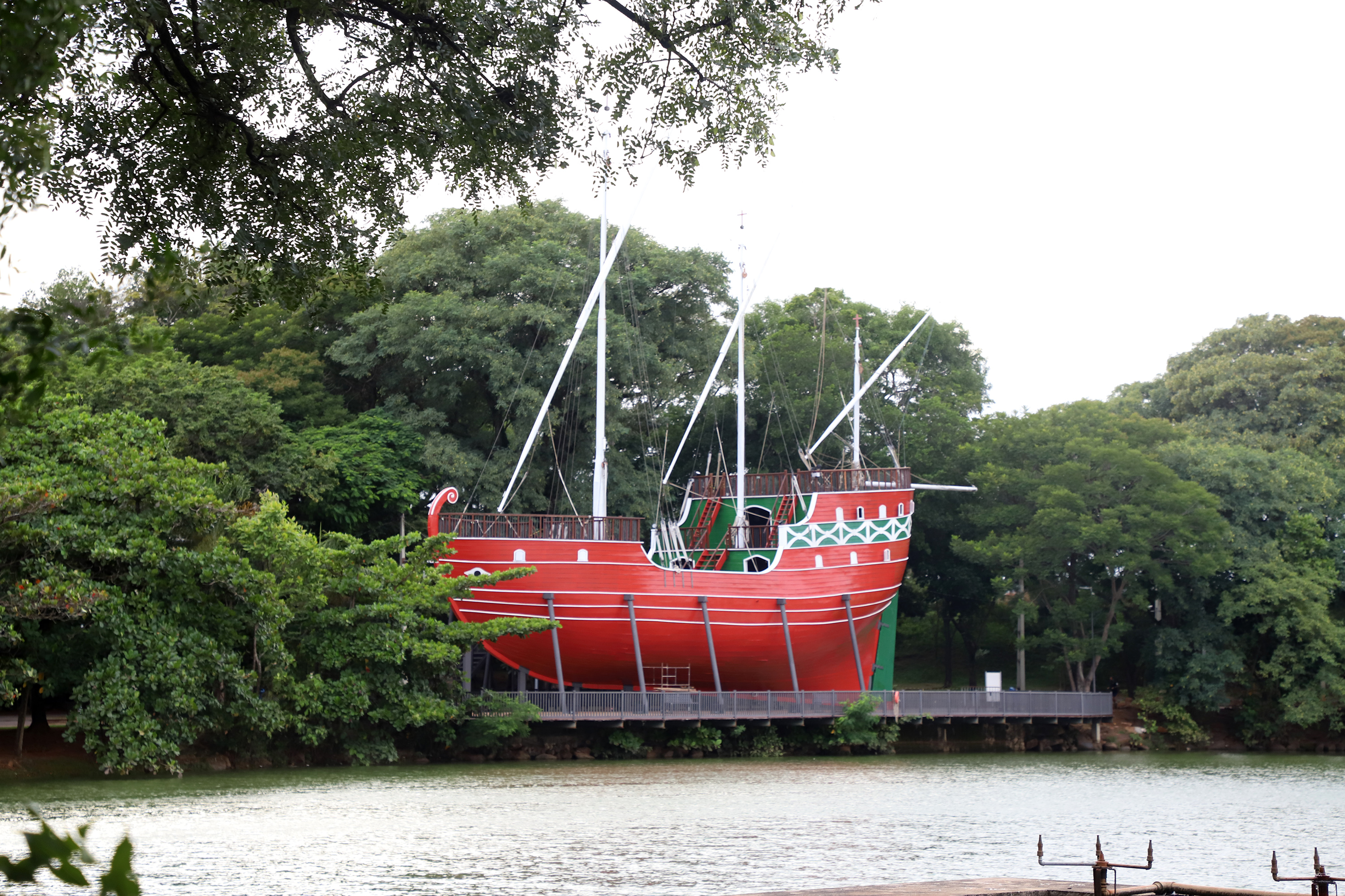 Réplica de caravela vermelha às margens da lagoa do Parque Taquaral, cercada por árvores