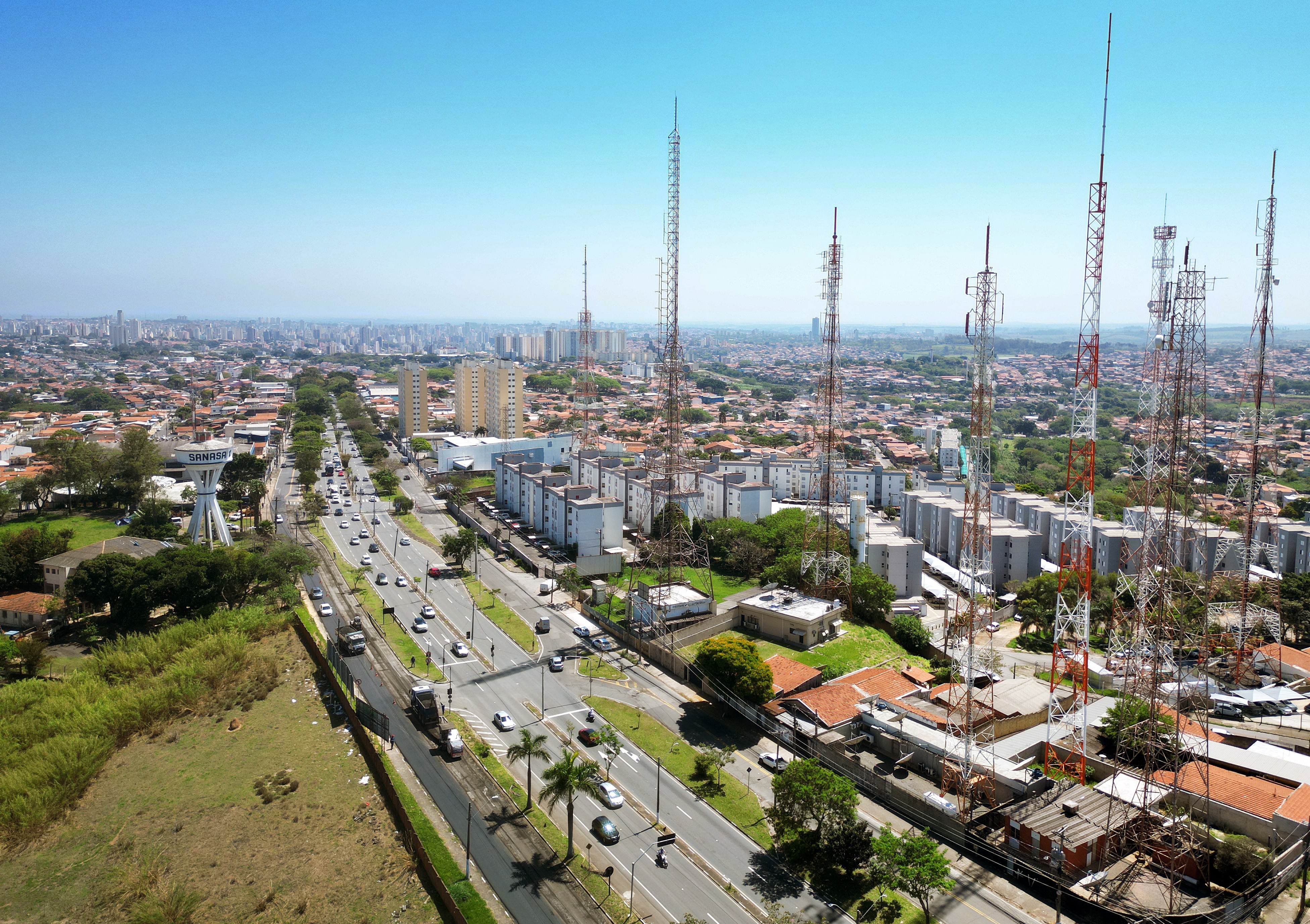 Panorama aéreo de Campinas com torres de transmissão, avenida arborizada e o centro da cidade no horizonte